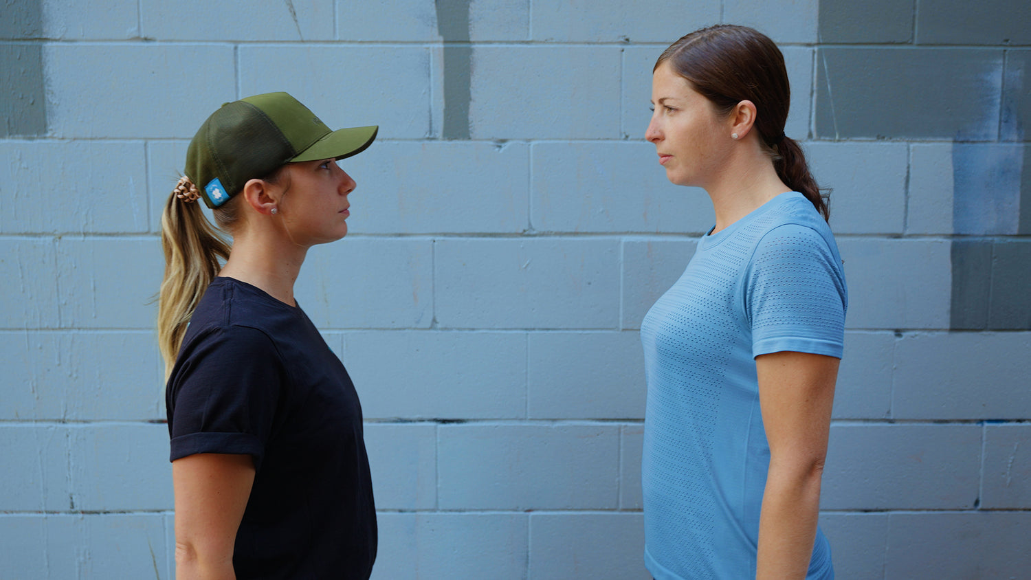 Two women in profile stand face-to face a few feet apart. In the background is a blue brick wall. video production videography videographer victoria bc