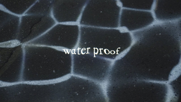 close-up of concrete pavement at night with water caustics projected onto the ground. Custom titles show the words "water proof" video production videography videographer victoria bc